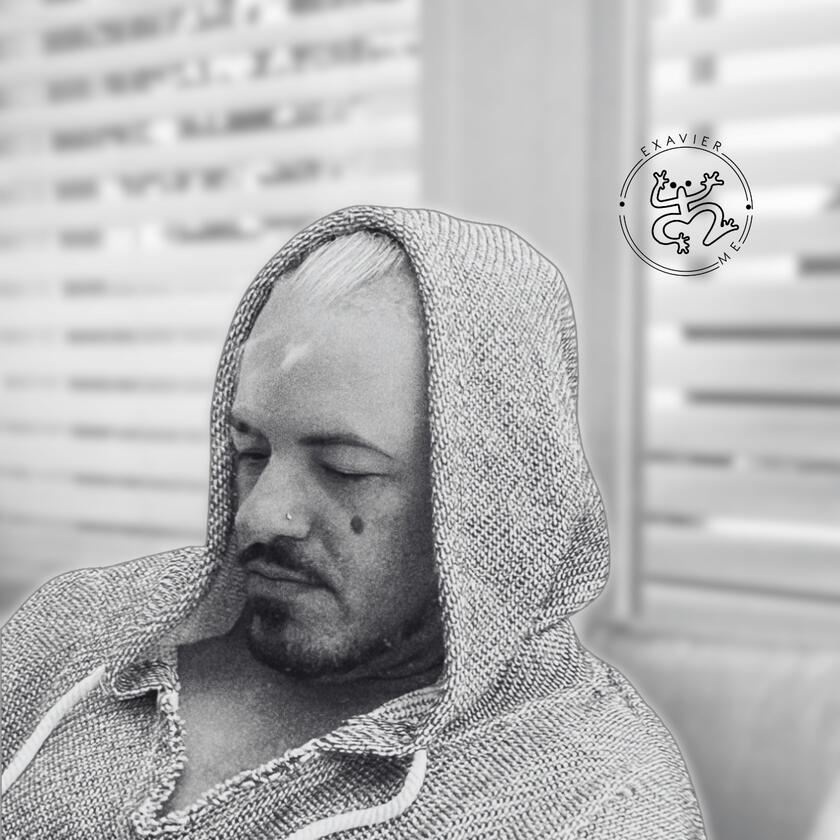 Black & White photo of Exavier Me sitting looking down while a hoody covers the back part of his head.